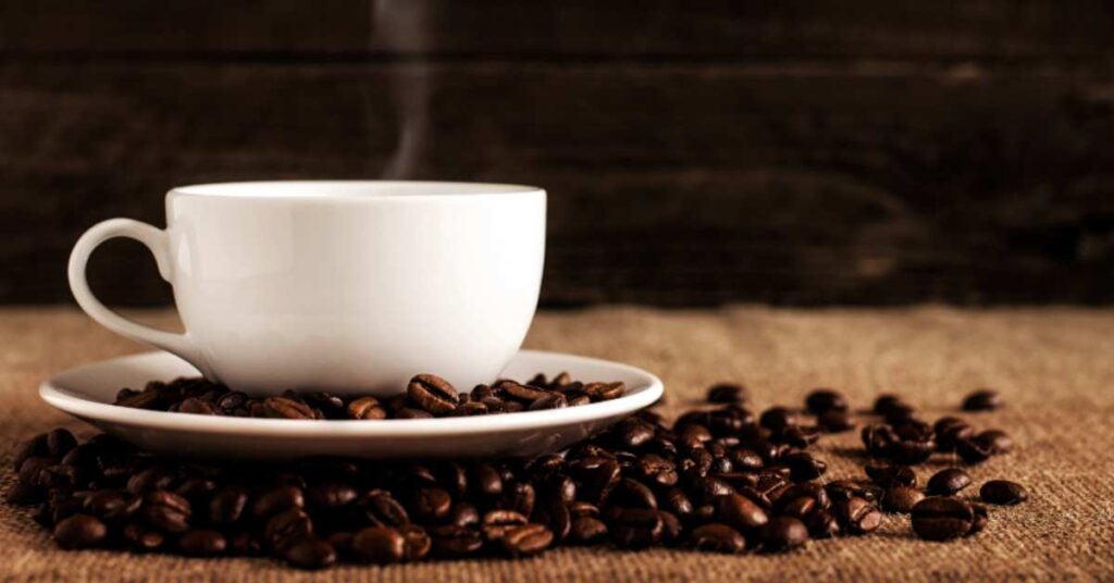 Steaming coffee mug sitting on plate surrounded by coffee beans